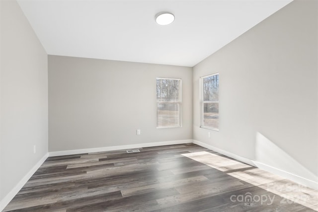 spare room featuring lofted ceiling, baseboards, and dark wood-type flooring