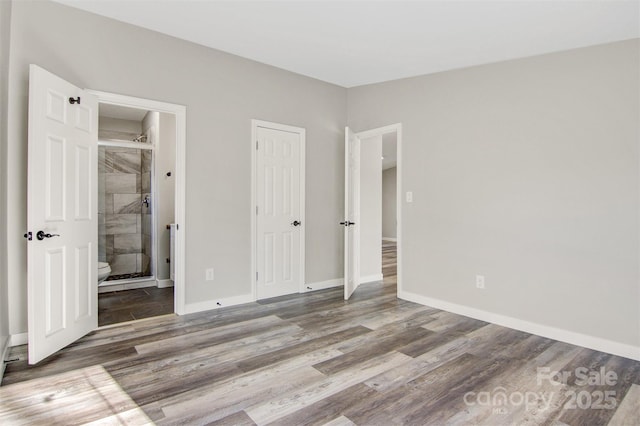 unfurnished bedroom with a closet, ensuite bathroom, baseboards, and wood finished floors