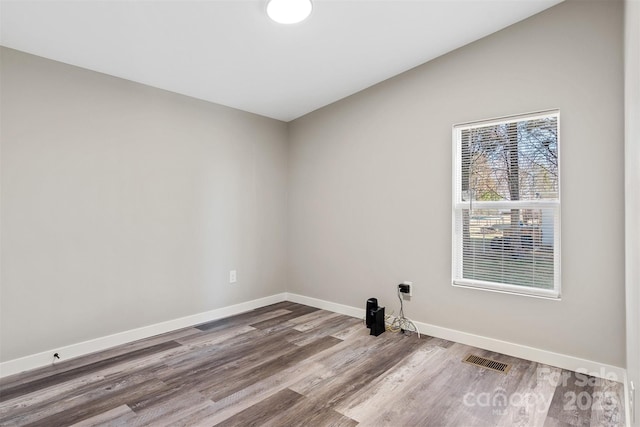 spare room featuring baseboards, visible vents, vaulted ceiling, and wood finished floors