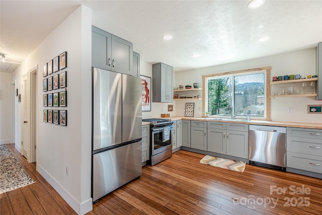 kitchen with sink, gray cabinetry, a textured ceiling, light hardwood / wood-style floors, and stainless steel appliances