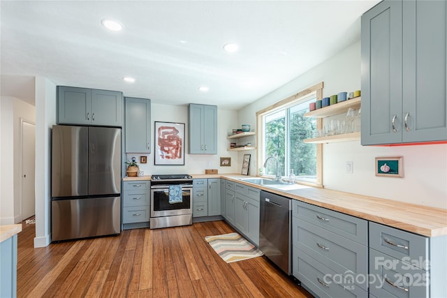 kitchen with appliances with stainless steel finishes, light hardwood / wood-style flooring, wooden counters, gray cabinetry, and sink