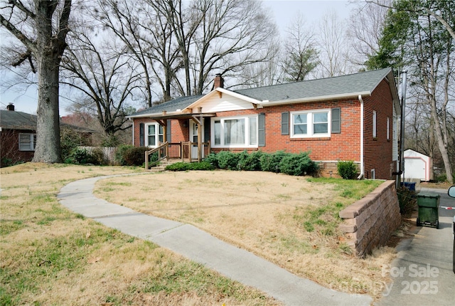 bungalow-style home with brick siding, a chimney, an outdoor structure, and a front yard