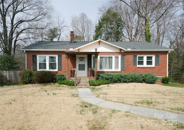 view of front facade featuring a front yard, brick siding, a chimney, and a shingled roof