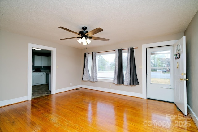 unfurnished living room featuring a textured ceiling, light wood-style flooring, baseboards, and ceiling fan