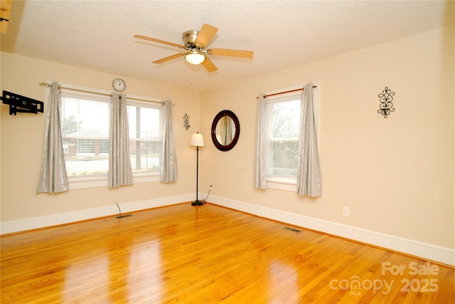 unfurnished room featuring light wood-type flooring, visible vents, a textured ceiling, and a ceiling fan