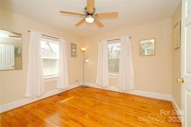 unfurnished room with visible vents, plenty of natural light, ceiling fan, and light wood finished floors