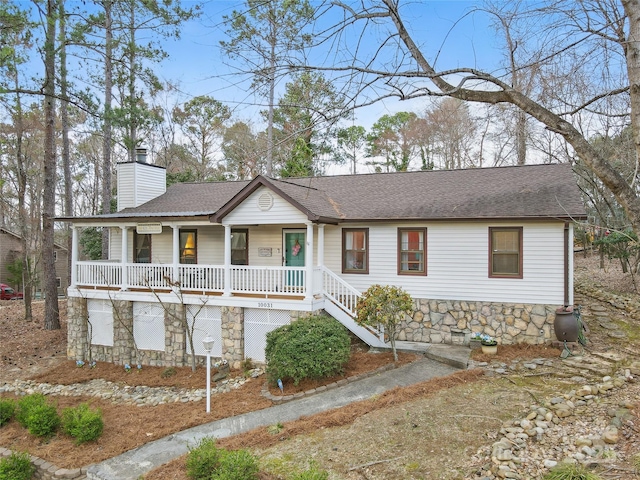 single story home featuring stone siding, a porch, a chimney, and roof with shingles