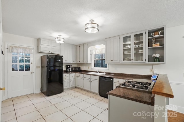 kitchen with black appliances, a sink, dark countertops, a peninsula, and glass insert cabinets