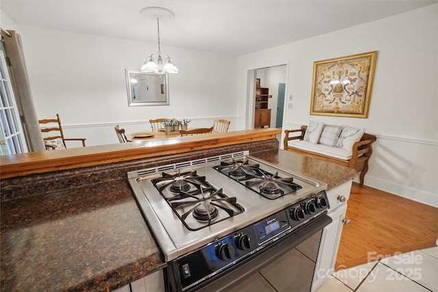 kitchen featuring dark countertops, a chandelier, range with gas stovetop, light wood-style floors, and hanging light fixtures