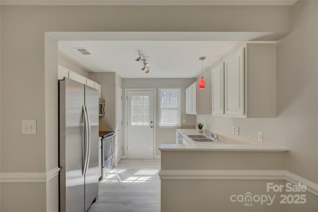 kitchen featuring a peninsula, a sink, white cabinets, light countertops, and appliances with stainless steel finishes