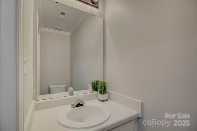 half bathroom featuring ornamental molding, visible vents, vanity, and toilet