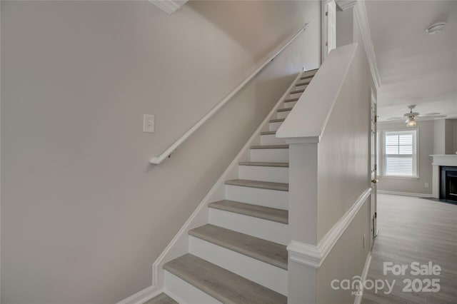 stairway featuring a fireplace with flush hearth, baseboards, and wood finished floors