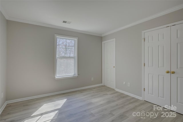 unfurnished bedroom featuring visible vents, baseboards, ornamental molding, a closet, and light wood-type flooring