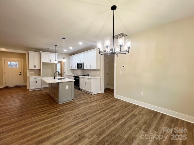 kitchen featuring an island with sink, hanging light fixtures, sink, range with electric cooktop, and white cabinets