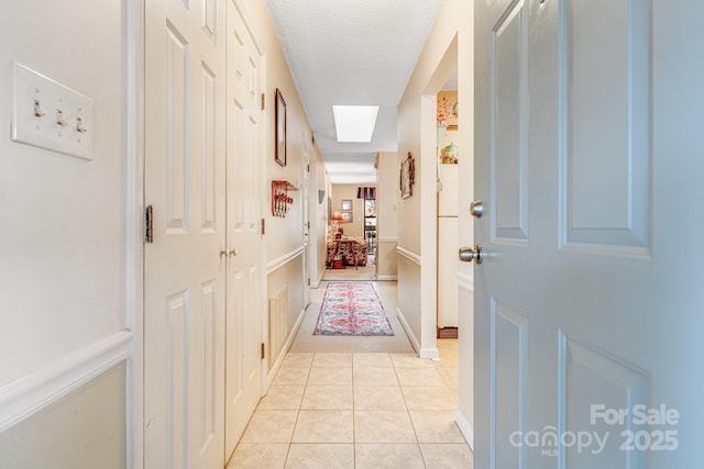 corridor featuring light tile patterned flooring, a textured ceiling, and a skylight