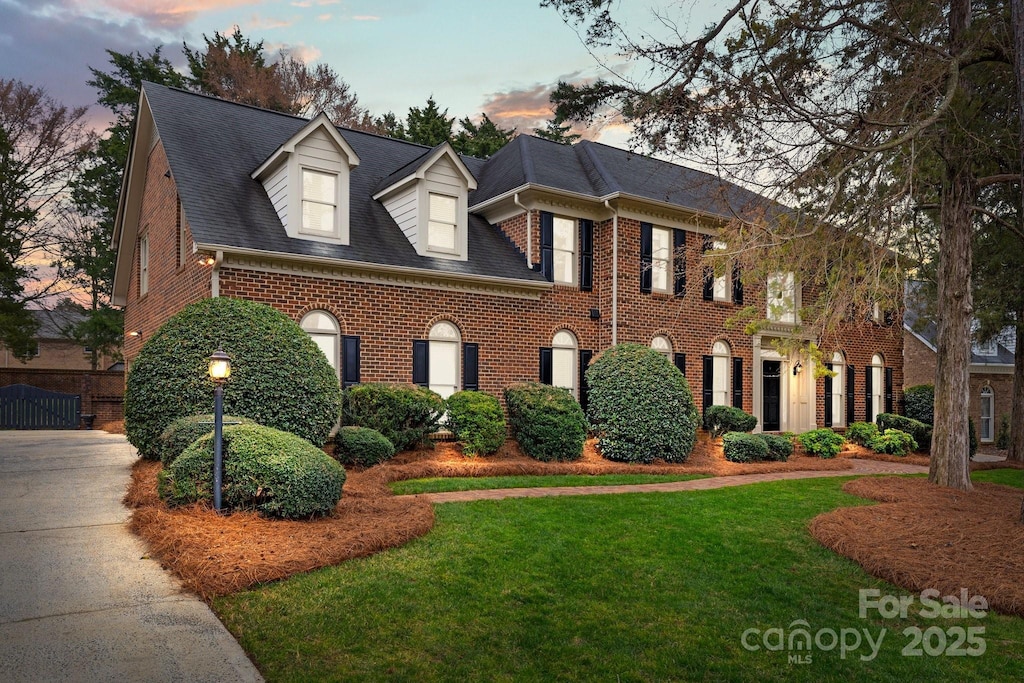 colonial home with brick siding, a lawn, and a shingled roof