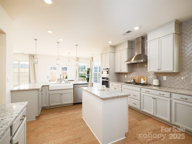 kitchen featuring light wood-style flooring, a kitchen island, appliances with stainless steel finishes, wall chimney range hood, and a sink