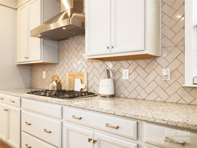 kitchen with light stone counters, white cabinetry, wall chimney exhaust hood, tasteful backsplash, and stainless steel gas stovetop