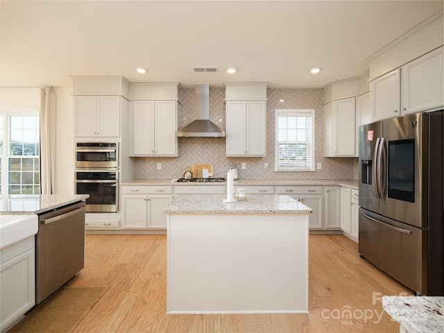 kitchen featuring light wood-type flooring, wall chimney exhaust hood, visible vents, and appliances with stainless steel finishes