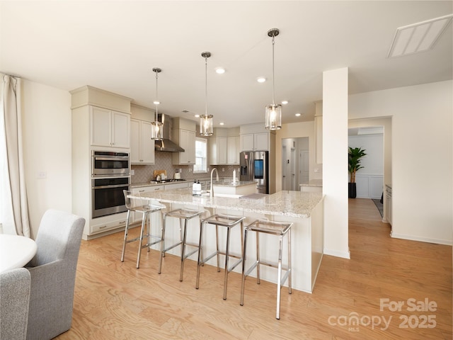 kitchen featuring stainless steel appliances, a kitchen breakfast bar, light wood-type flooring, decorative backsplash, and wall chimney exhaust hood