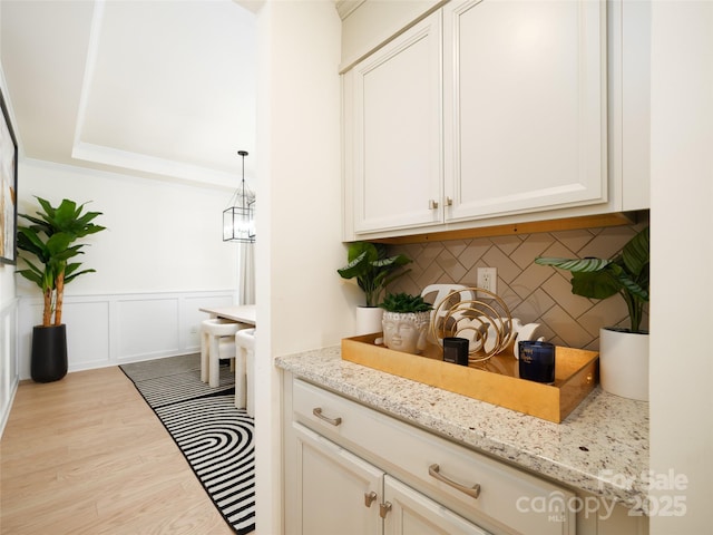 bar featuring decorative backsplash, wainscoting, wood finished floors, hanging light fixtures, and a decorative wall