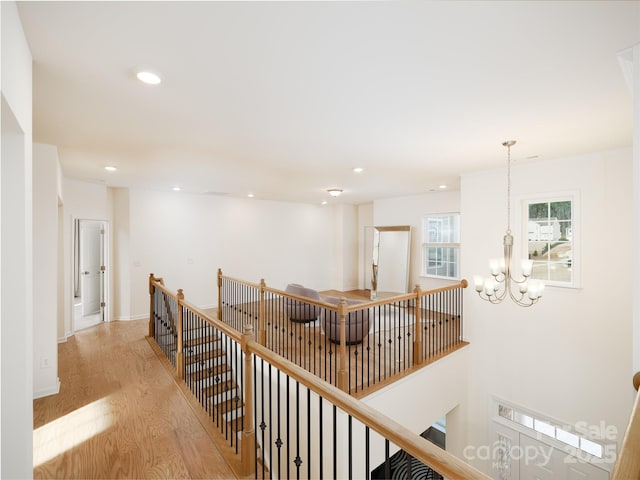 hallway with baseboards, light wood-style flooring, an upstairs landing, a chandelier, and recessed lighting