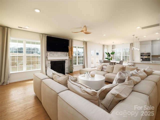 living room featuring light wood finished floors, recessed lighting, visible vents, and a stone fireplace