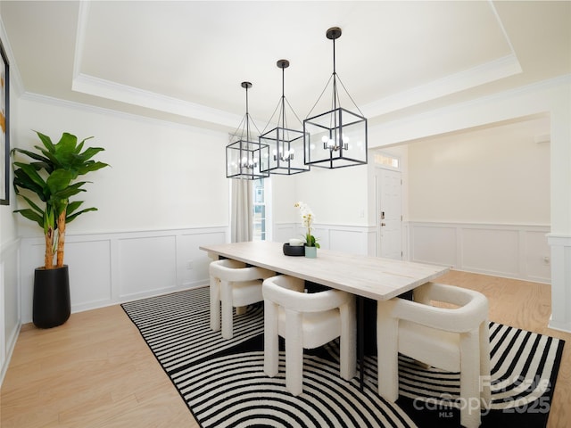 dining space featuring light wood-type flooring, a raised ceiling, and crown molding