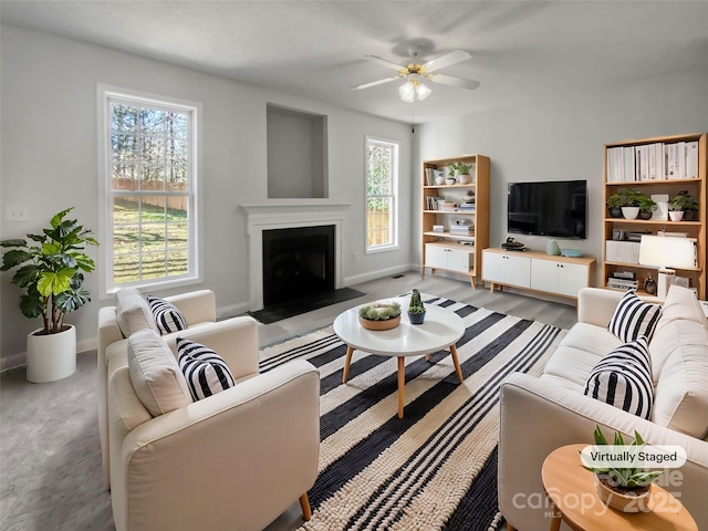 living area featuring a fireplace with flush hearth, a ceiling fan, and baseboards