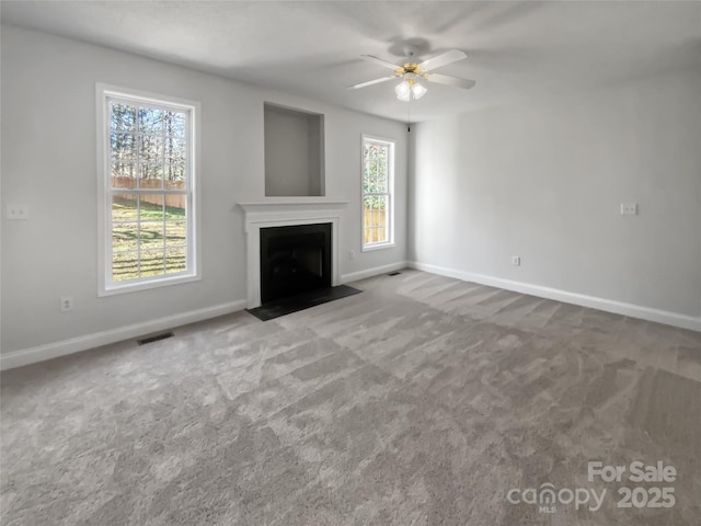 unfurnished living room featuring carpet, visible vents, a fireplace with flush hearth, ceiling fan, and baseboards