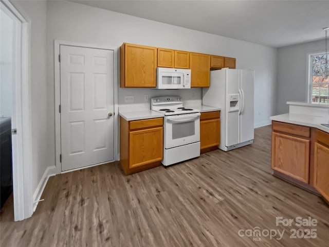 kitchen featuring light countertops, light wood-style floors, brown cabinetry, white appliances, and baseboards