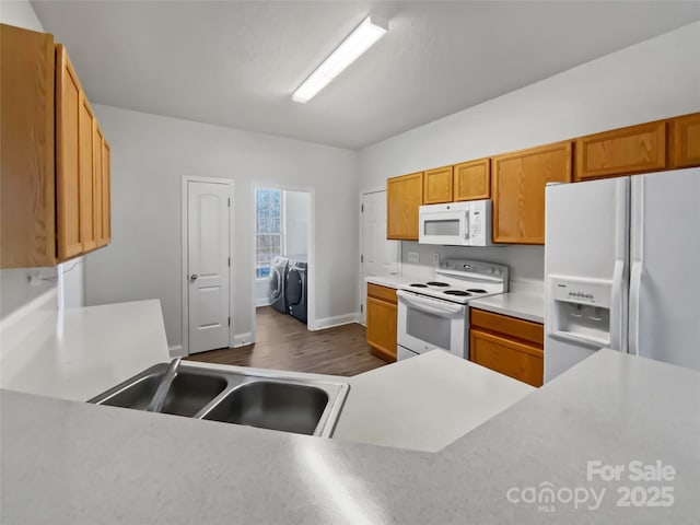 kitchen with dark wood-style flooring, washing machine and clothes dryer, light countertops, a sink, and white appliances