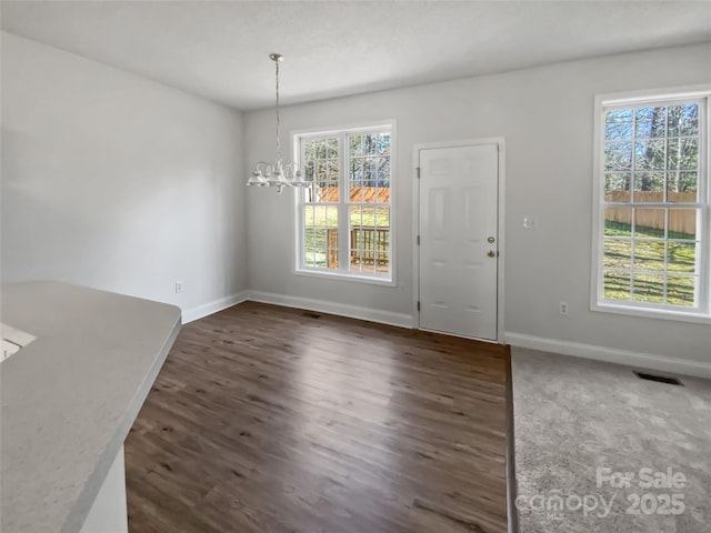 unfurnished dining area featuring baseboards, dark wood-style flooring, visible vents, and a notable chandelier