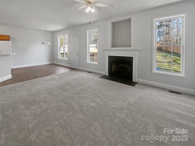 unfurnished living room with carpet, a fireplace with flush hearth, baseboards, and ceiling fan with notable chandelier