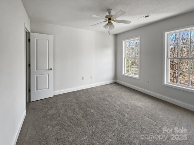 spare room featuring ceiling fan, a textured ceiling, visible vents, baseboards, and dark colored carpet