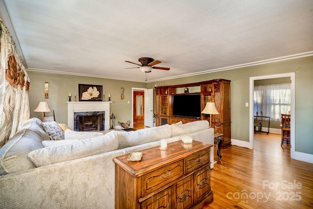 living area with a ceiling fan, a high end fireplace, baseboards, light wood finished floors, and crown molding