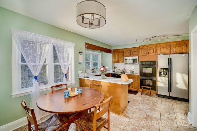 kitchen featuring a peninsula, brown cabinetry, light tile patterned floors, and stainless steel appliances