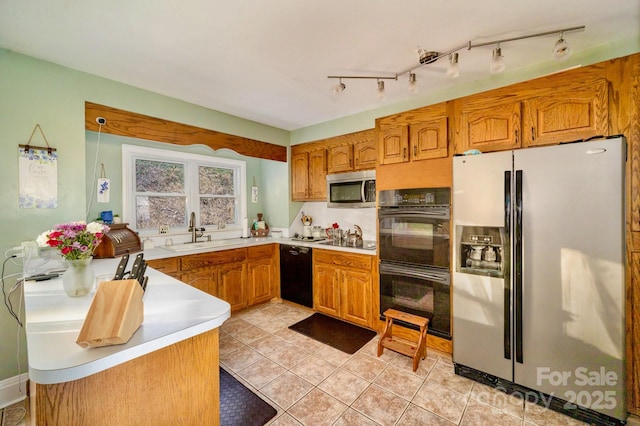 kitchen with light tile patterned floors, brown cabinets, light countertops, black appliances, and a sink