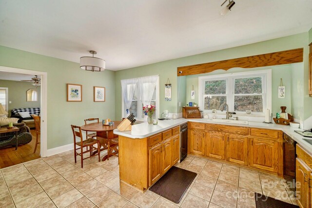 kitchen with light tile patterned floors, a peninsula, a sink, light countertops, and brown cabinets