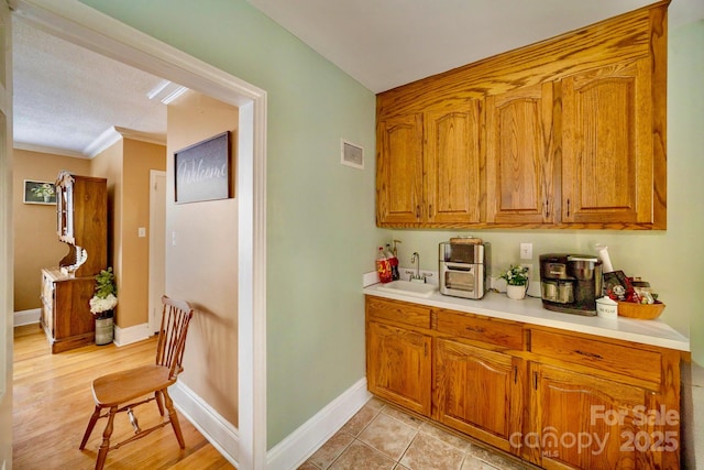 kitchen with light countertops, brown cabinetry, a sink, and baseboards