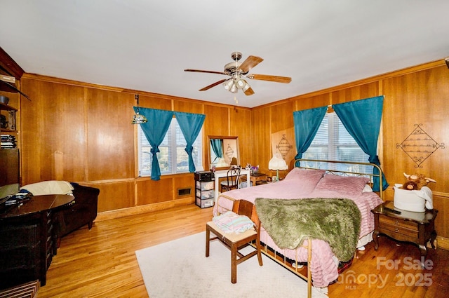 bedroom with ceiling fan, wooden walls, visible vents, and wood finished floors