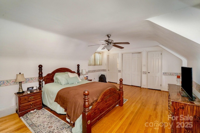 bedroom featuring vaulted ceiling, light wood-type flooring, a ceiling fan, and multiple closets