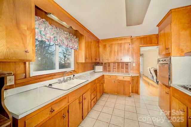 kitchen featuring light tile patterned floors, oven, a sink, light countertops, and brown cabinets