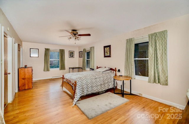 bedroom featuring a baseboard heating unit, wood finished floors, a ceiling fan, and baseboards