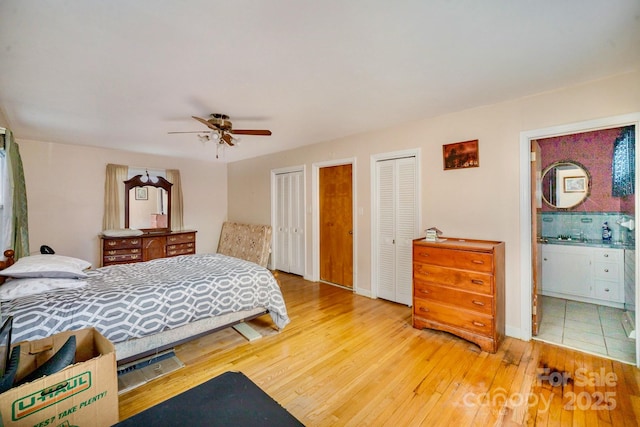 bedroom with two closets, hardwood / wood-style floors, ensuite bathroom, ceiling fan, and baseboards