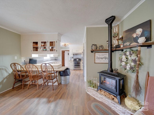 dining area with a wood stove, a textured ceiling, crown molding, and light hardwood / wood-style flooring