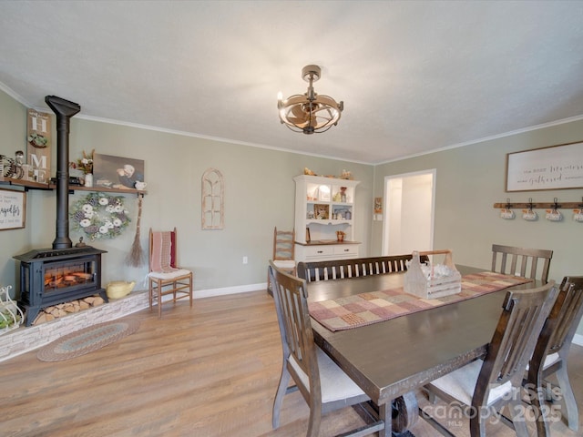 dining room featuring a notable chandelier, ornamental molding, a wood stove, and light hardwood / wood-style floors