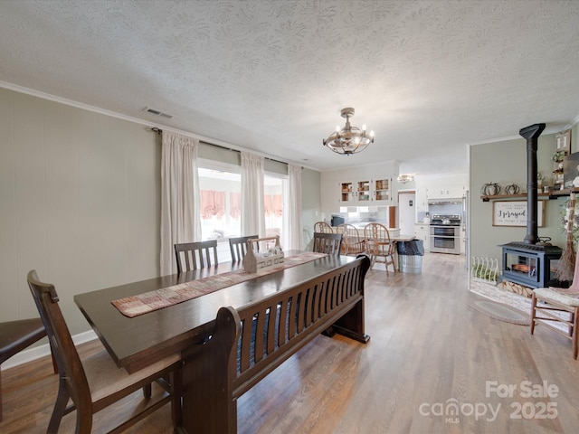 dining area featuring an inviting chandelier, ornamental molding, light hardwood / wood-style flooring, a wood stove, and a textured ceiling