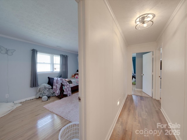 corridor with ornamental molding, a textured ceiling, and light hardwood / wood-style floors