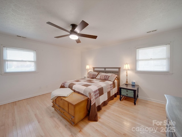 bedroom with ceiling fan, a textured ceiling, light wood-type flooring, and multiple windows